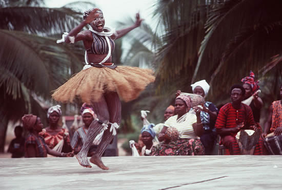 An African woman, wearing native garments, performs during a visit from participants in the West Africa Training Cruise 1983. Photo from April 1984 All Hands Magazine.